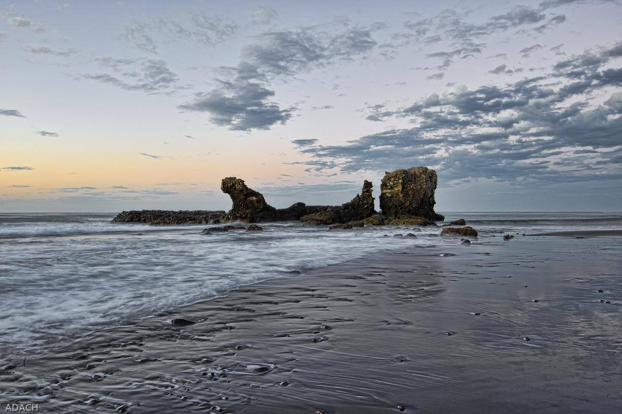 The rock formation at El Tunco beach at dusk, with waves washing over dark volcanic sand